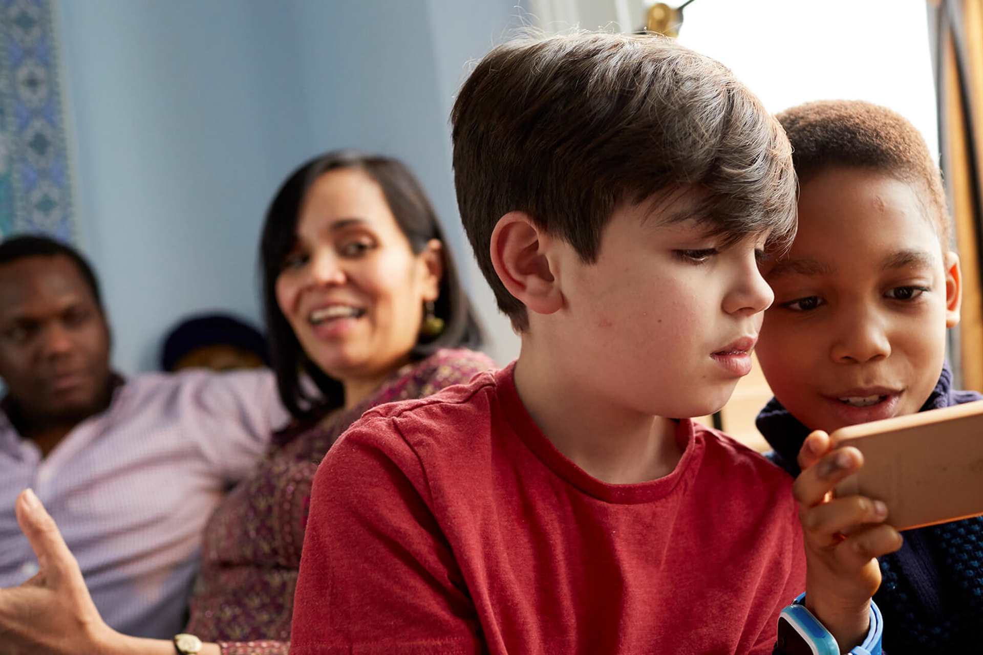 A family relaxing at home with parents chatting and children playing on a tablet