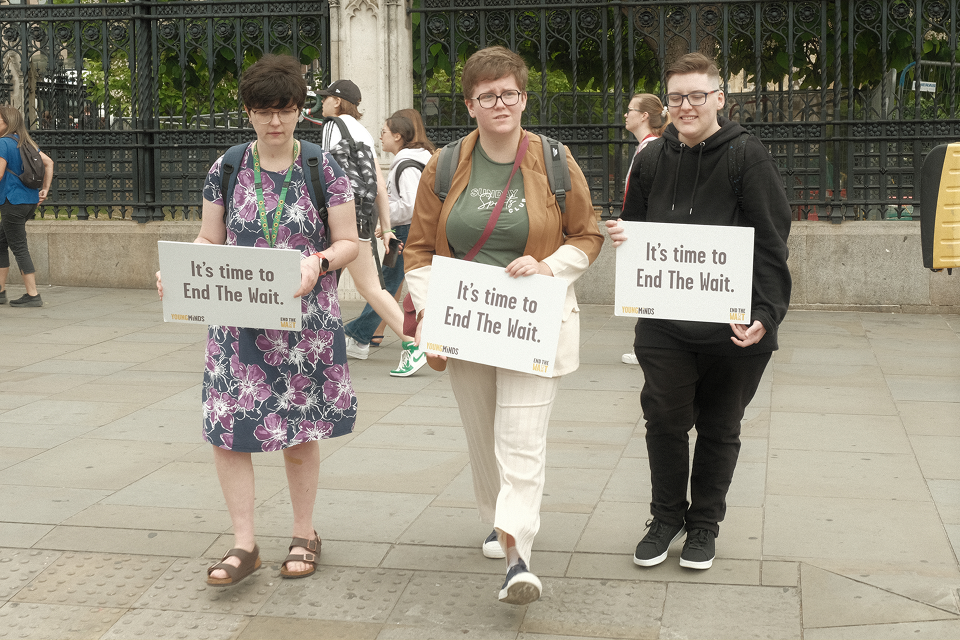 Three Activists holding signs in Parliament Square that read: "It's time to End The Wait."