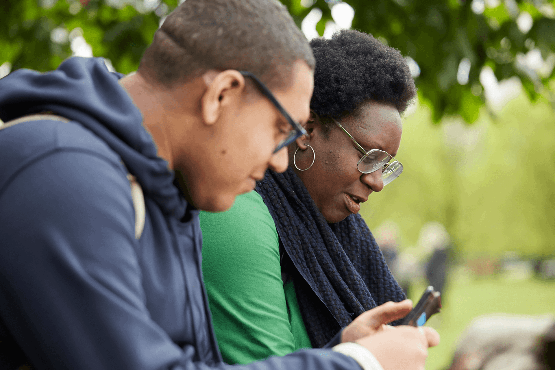 Two people sitting in a park using their mobile phones.