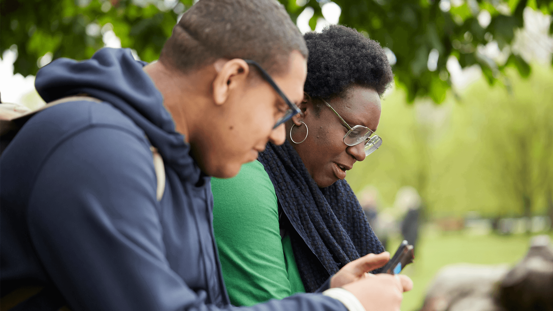 Two people sitting in a park using their mobile phones.