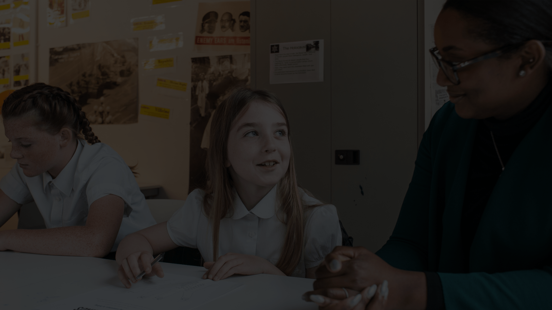  A teacher is smiling to her student who is sitting at a desk and working.