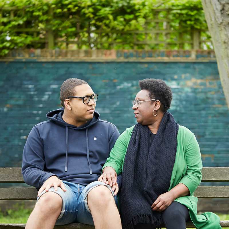 A mother and son holding hands on a bench looking at each other