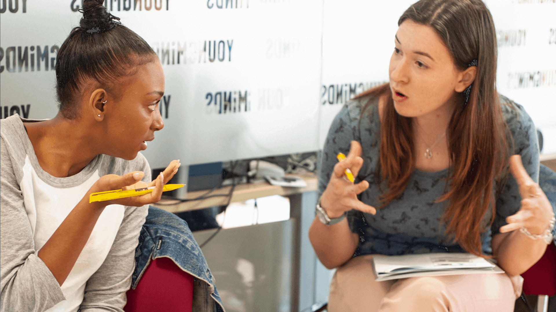 two moms are having a discussion over an activity while sitting on chairs inside a conference room