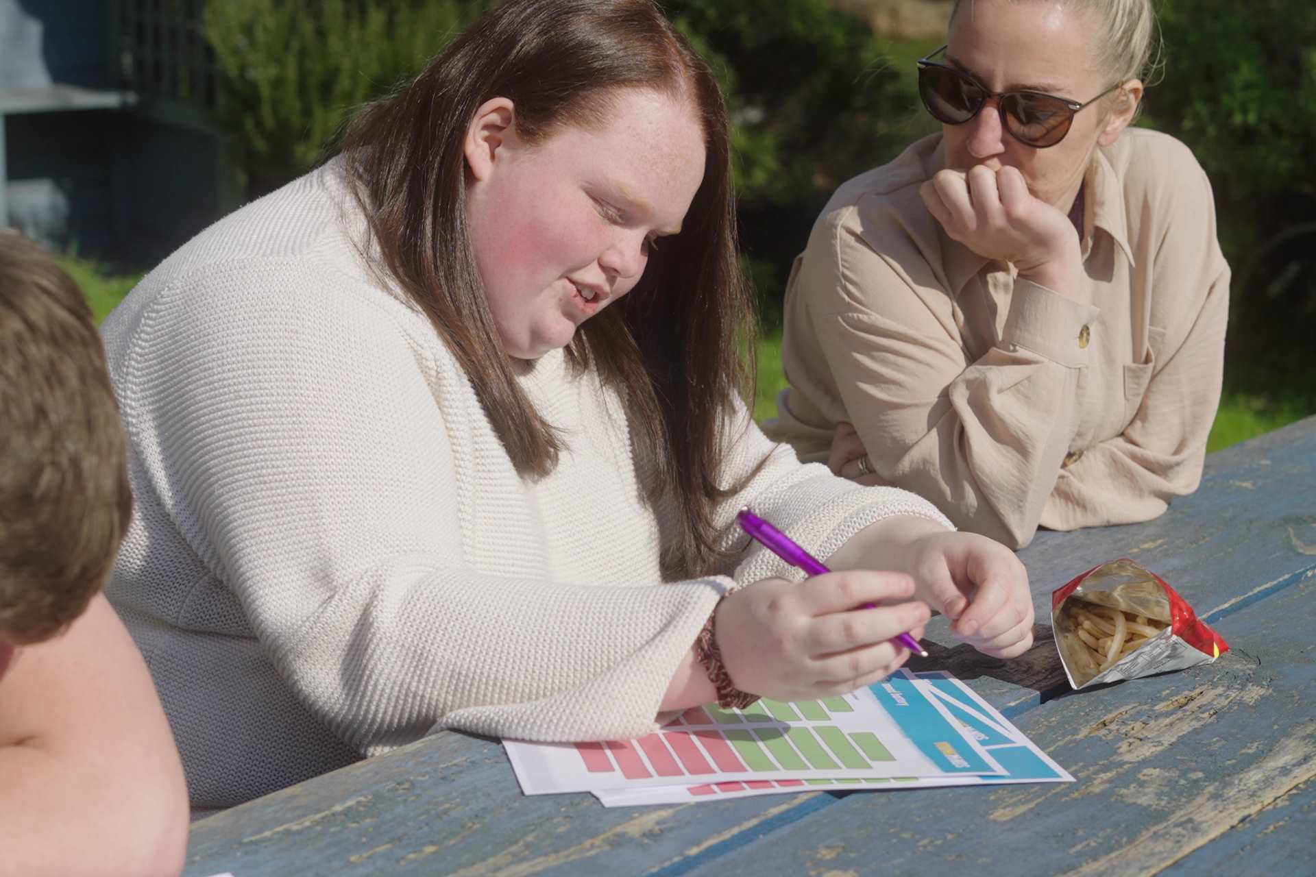 girl writing on mood battery resource with youth worker outside