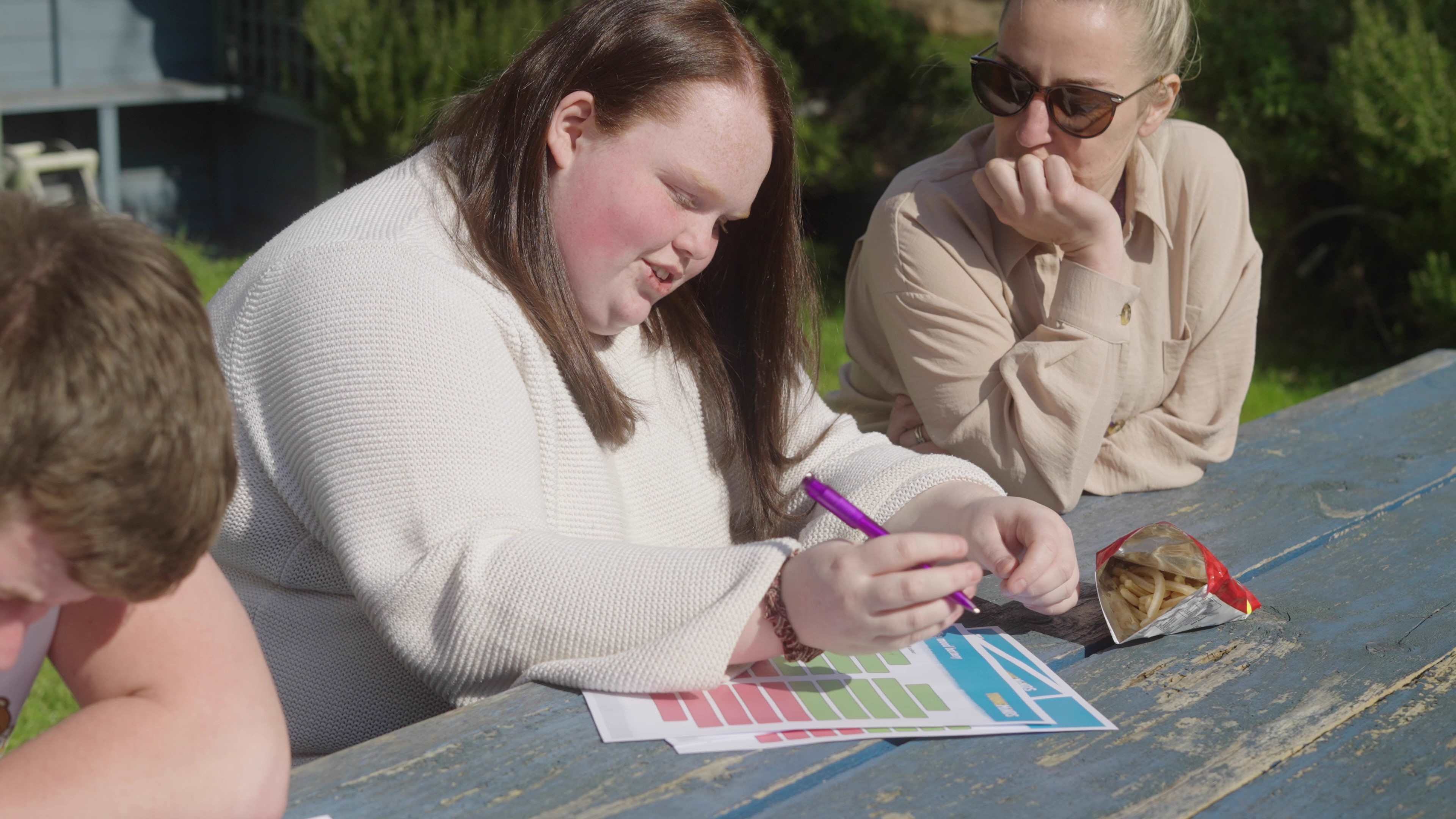 girl writing on mood battery resource with youth worker outside