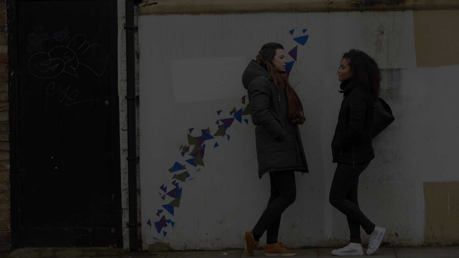 Two young people talking against a brick wall