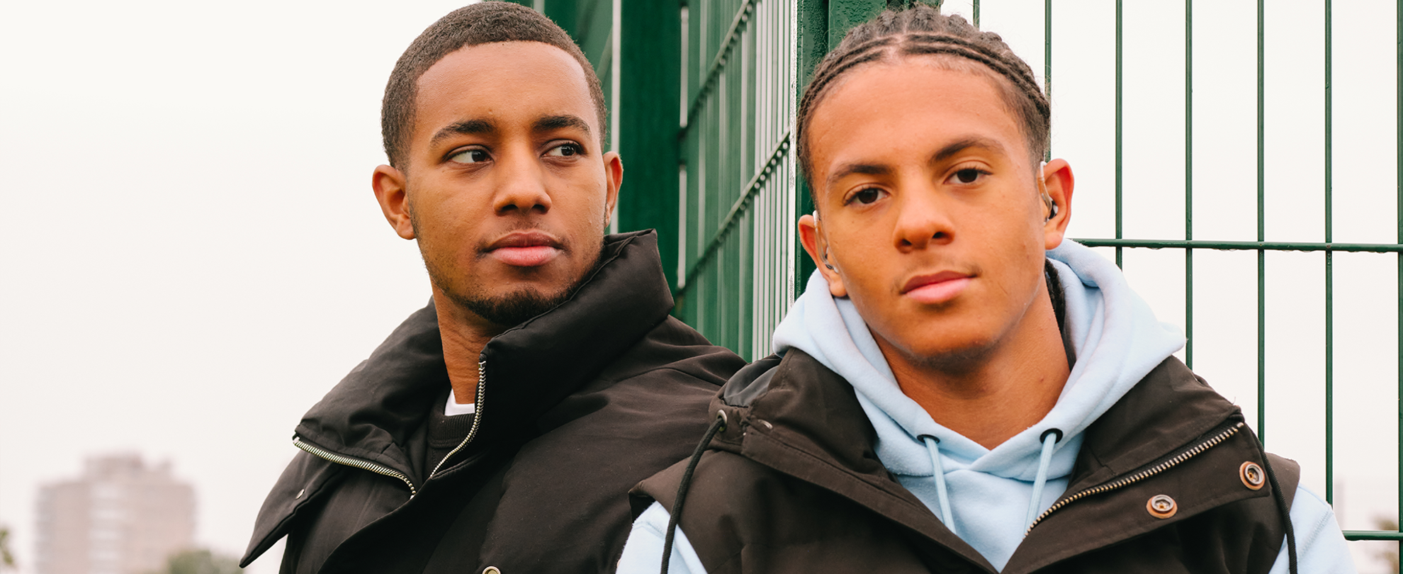 A young Black man sitting in the park with a Black teenage boy wearing a hearing aid. They are both looking very serious.