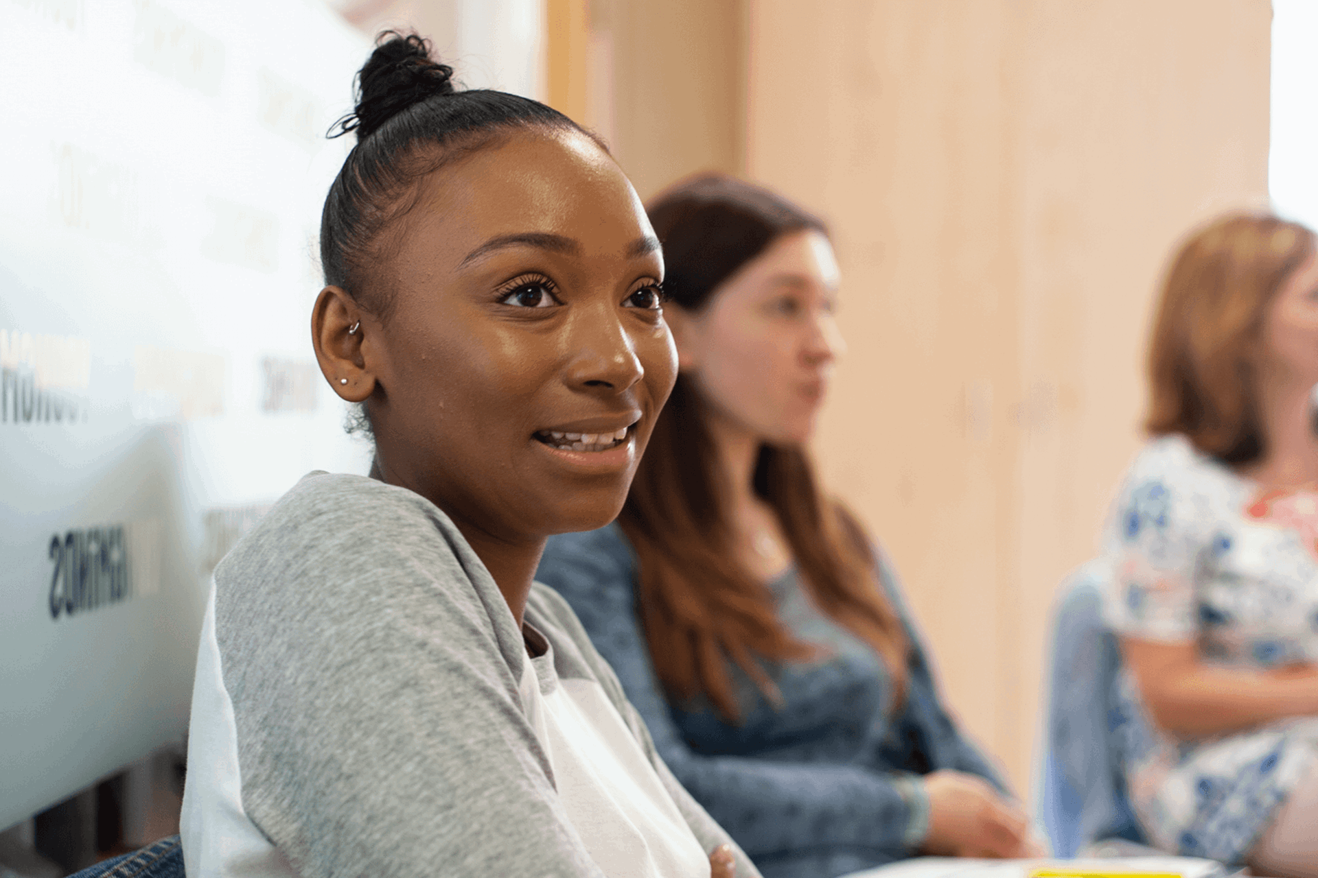 A young woman talking during a parents group session. Two mums are sitting and listening on the background.