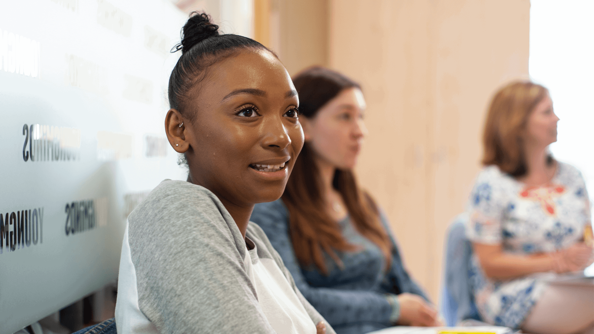 A young woman talking during a parents group session. Two mums are sitting and listening on the background.