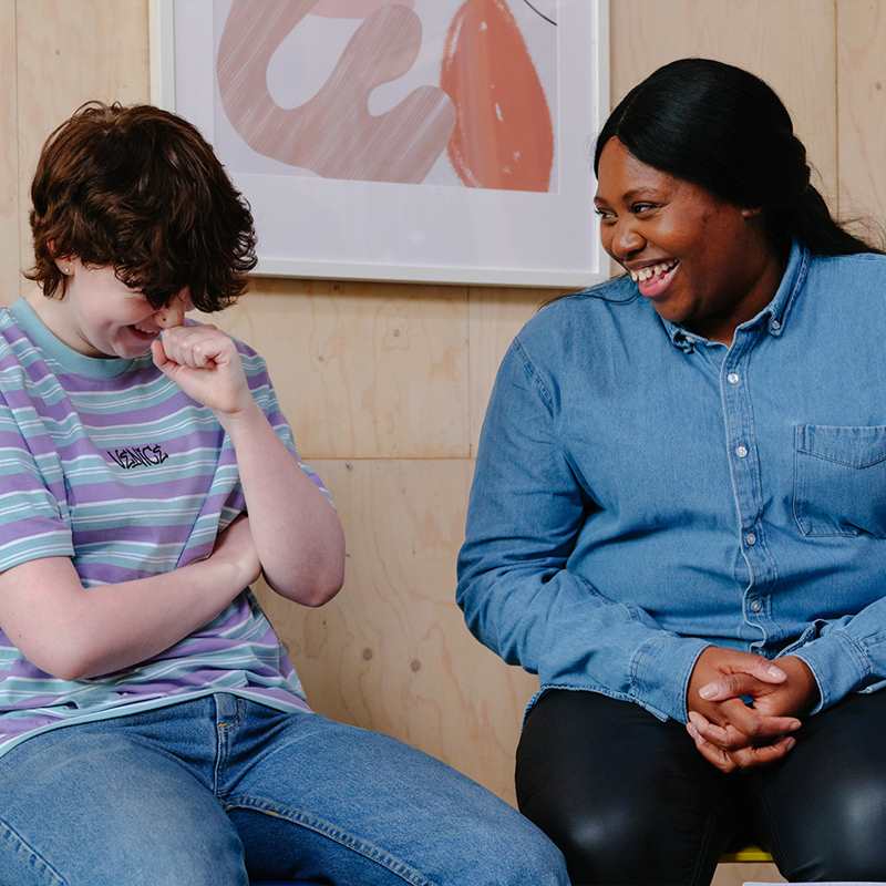 A white non-binary teenager laughing with an older Black woman in a professional setting.