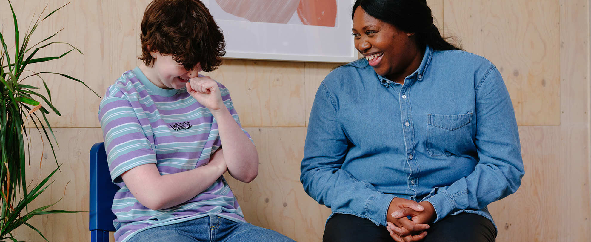 A white non-binary teenager laughing with an older Black woman in a professional setting.