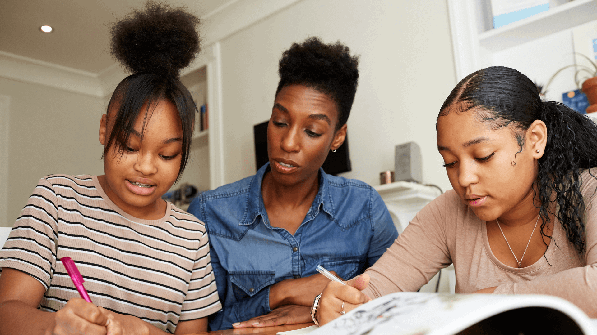 A close up of a mother and her daughters doing homework together in the lounge