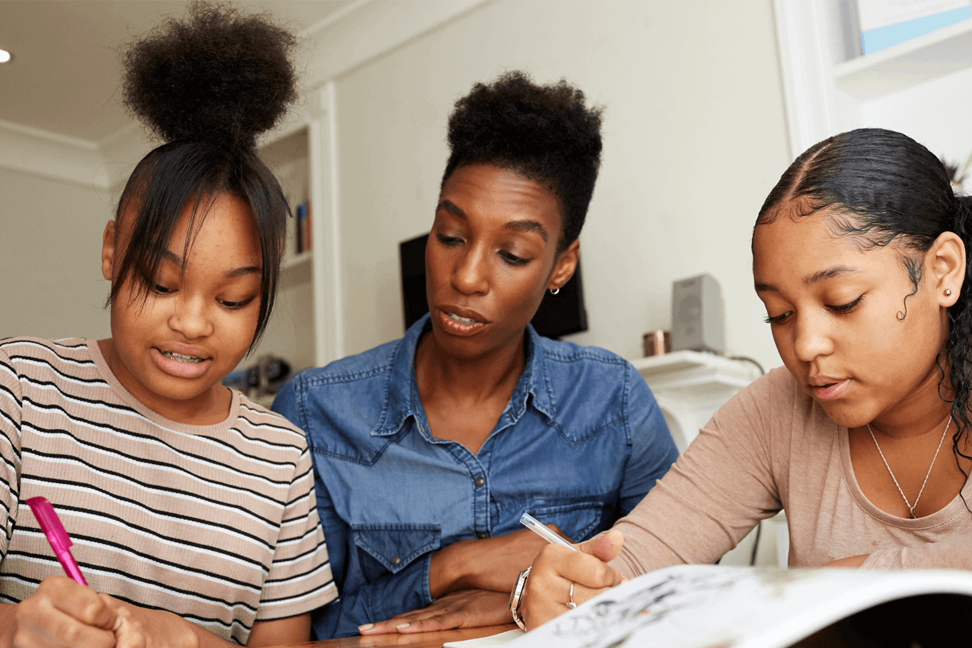 A close up of a mother and her daughters doing homework together in the lounge