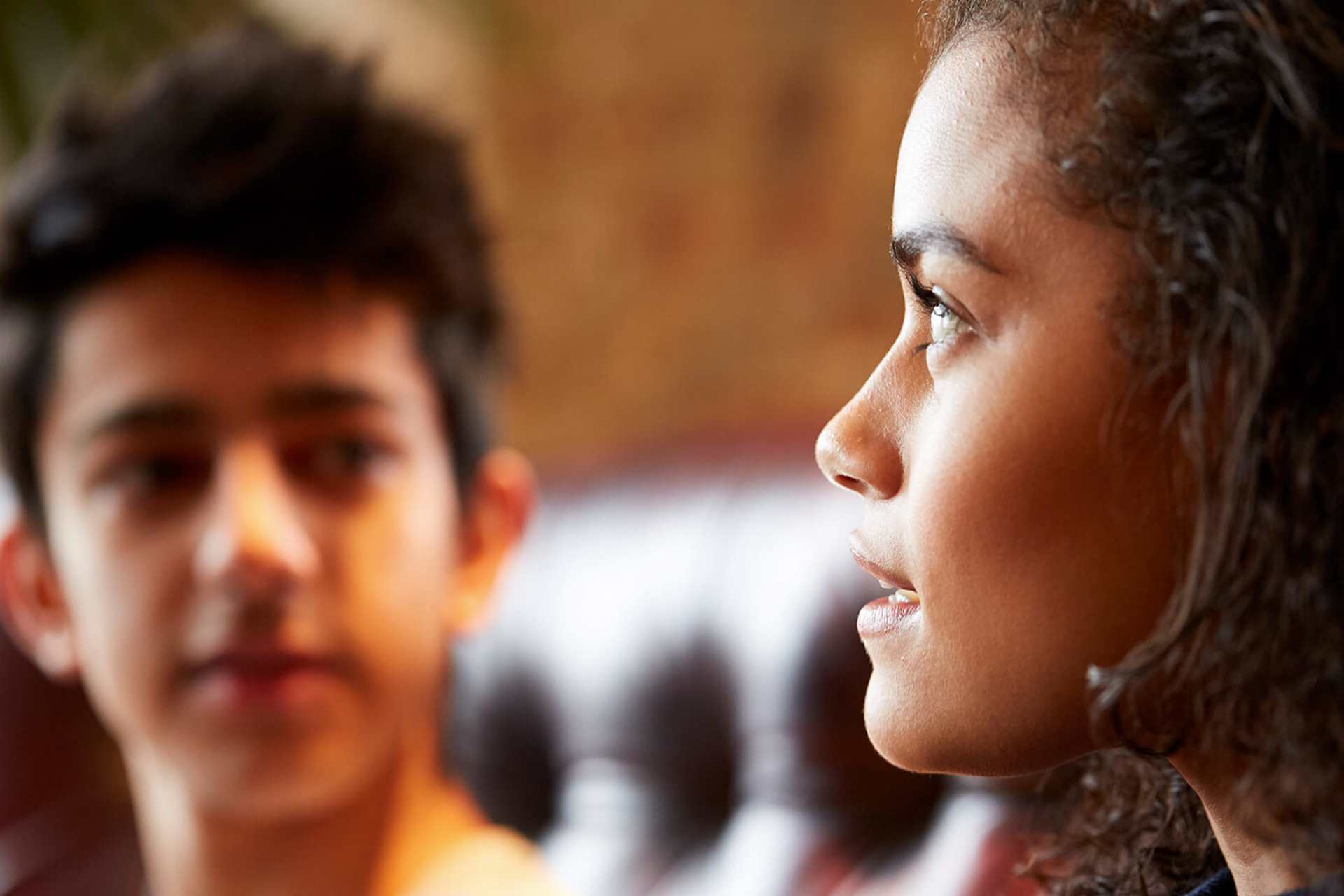 close-up-of-a-young-woman-talking-while-looking-away-and-a-young-man-on-background-looking-at-the-girl-while-she-talks