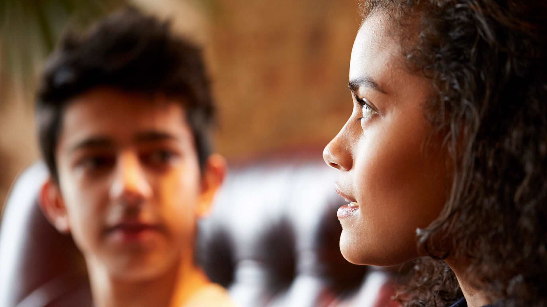 close-up-of-a-young-woman-talking-while-looking-away-and-a-young-man-on-background-looking-at-the-girl-while-she-talks