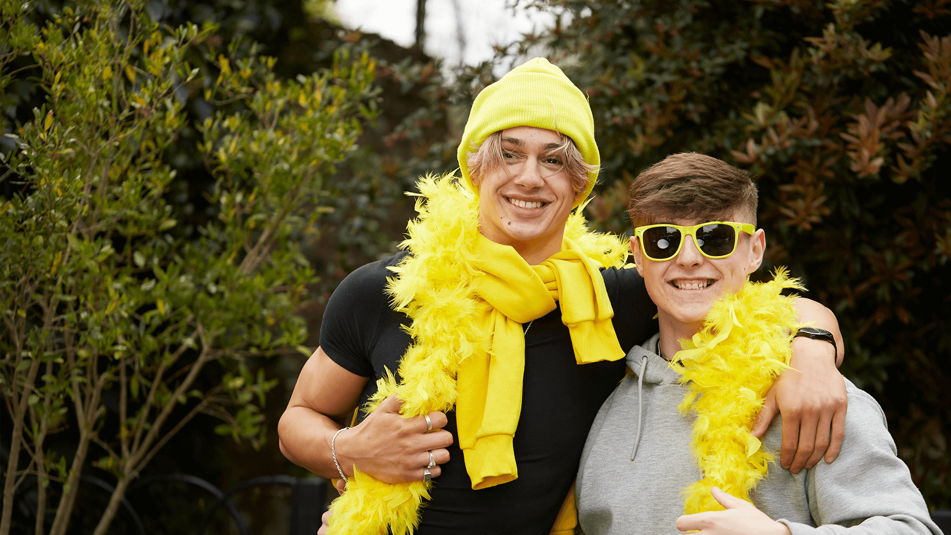 An image of two boys dressed up with yellow feather boas, a yellow hat and yellow sunglasses
