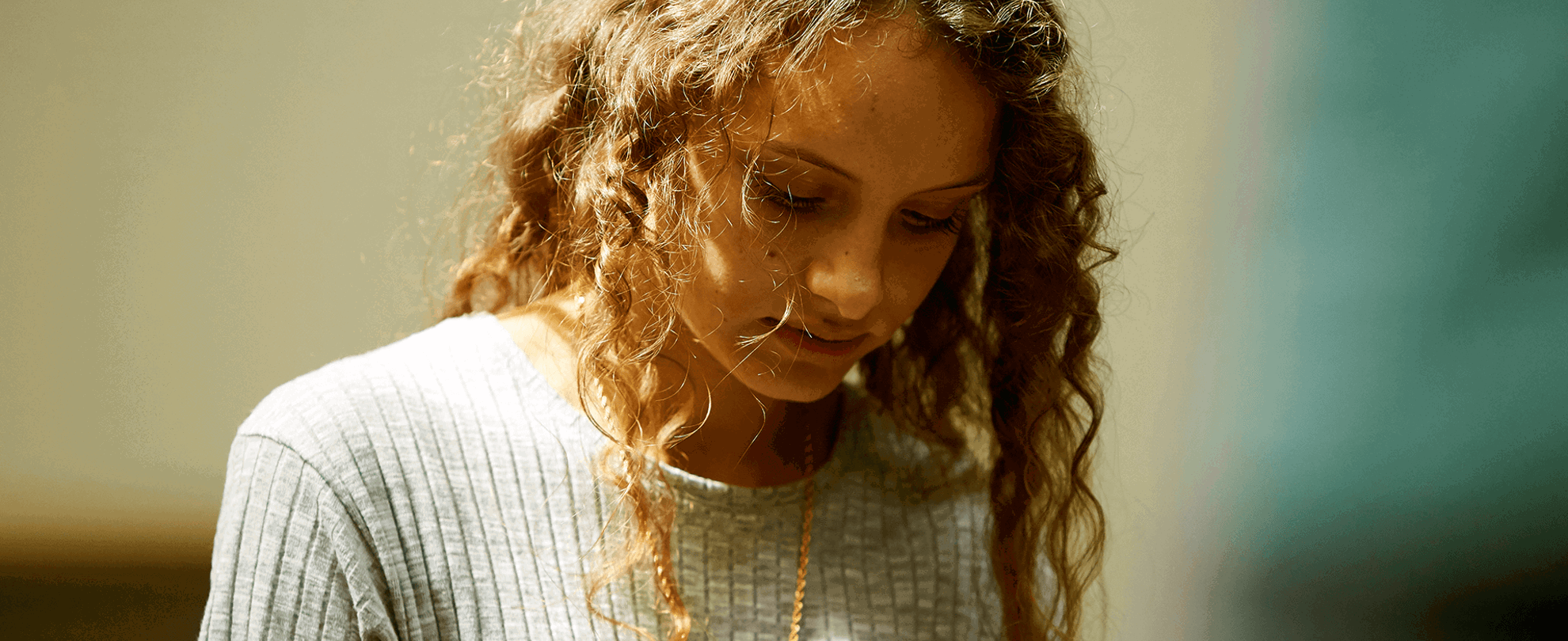 A young person alone and looking down at the ground.