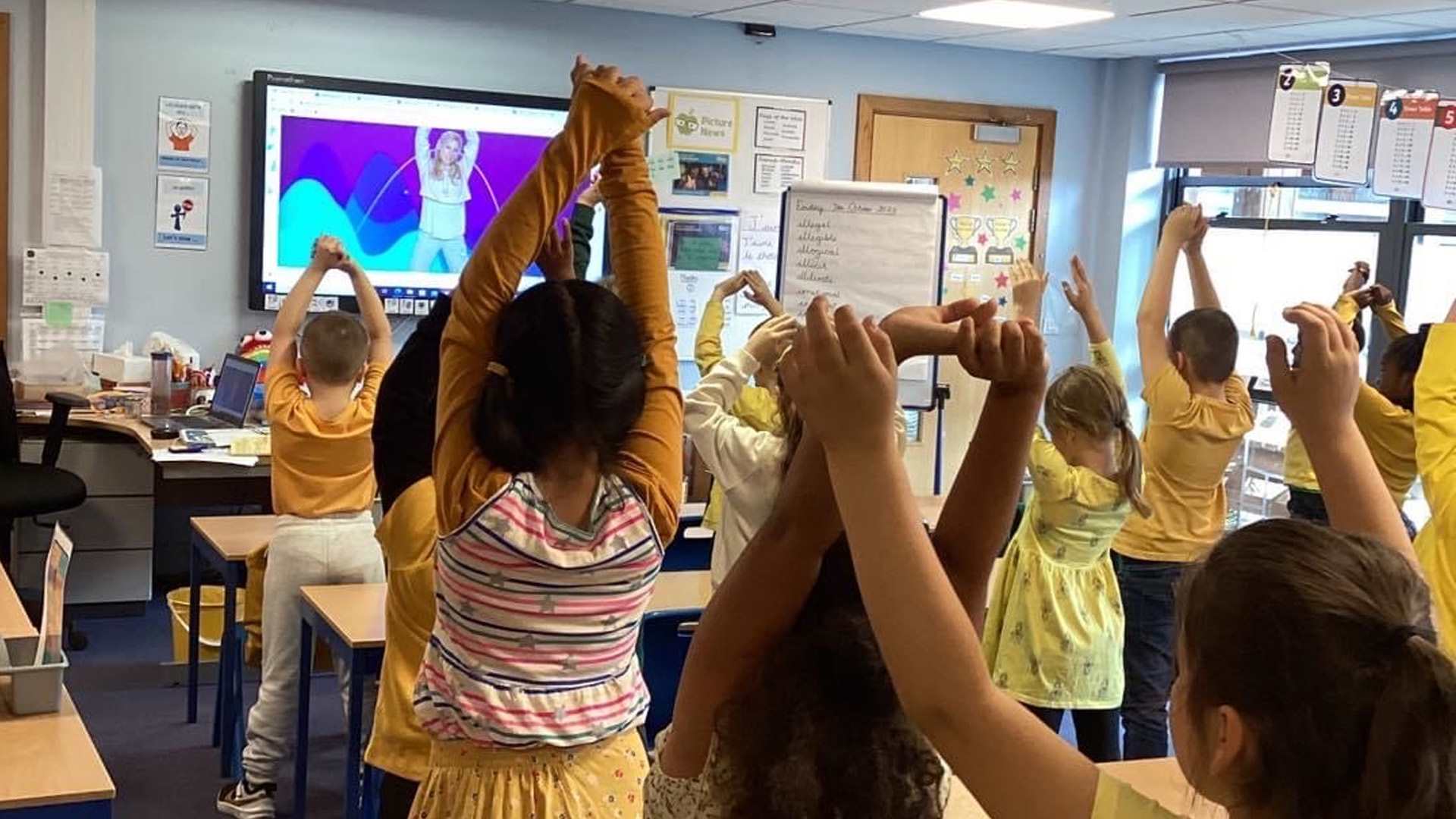 A class of primary school students stretching with their hands in the air all wearing yellow.