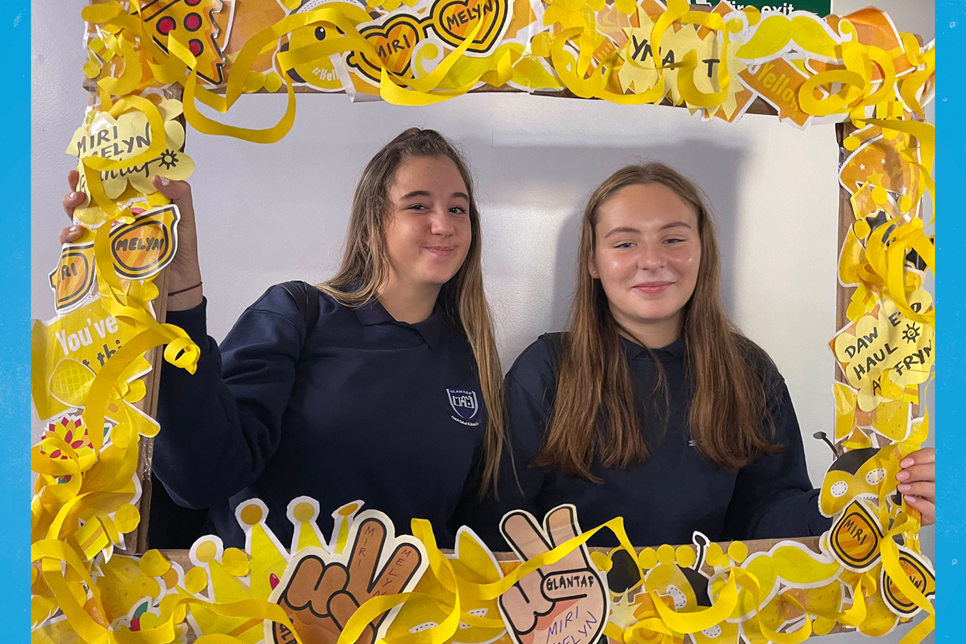 Two students from Ysgol Glantaf holding up a yellow frame and smiling.