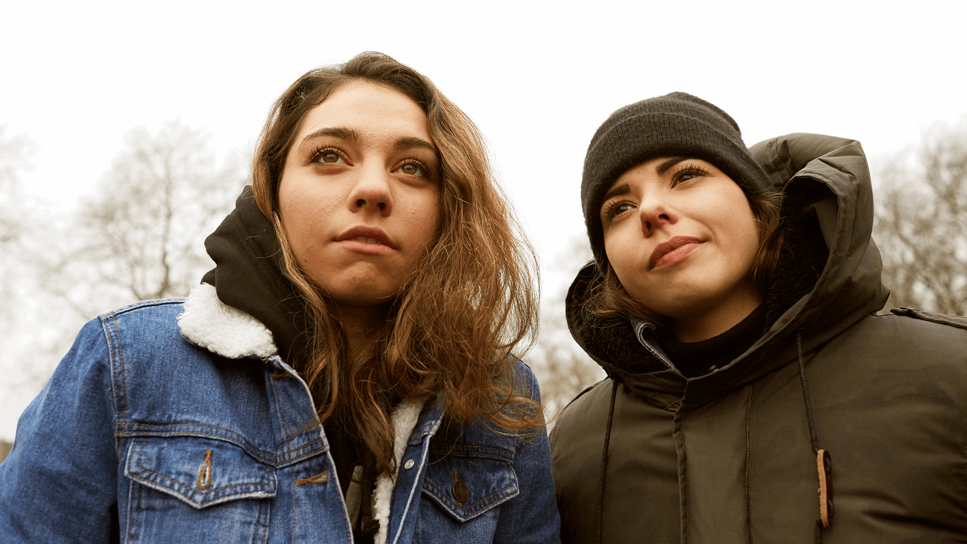 Two young people standing together and looking up at something.