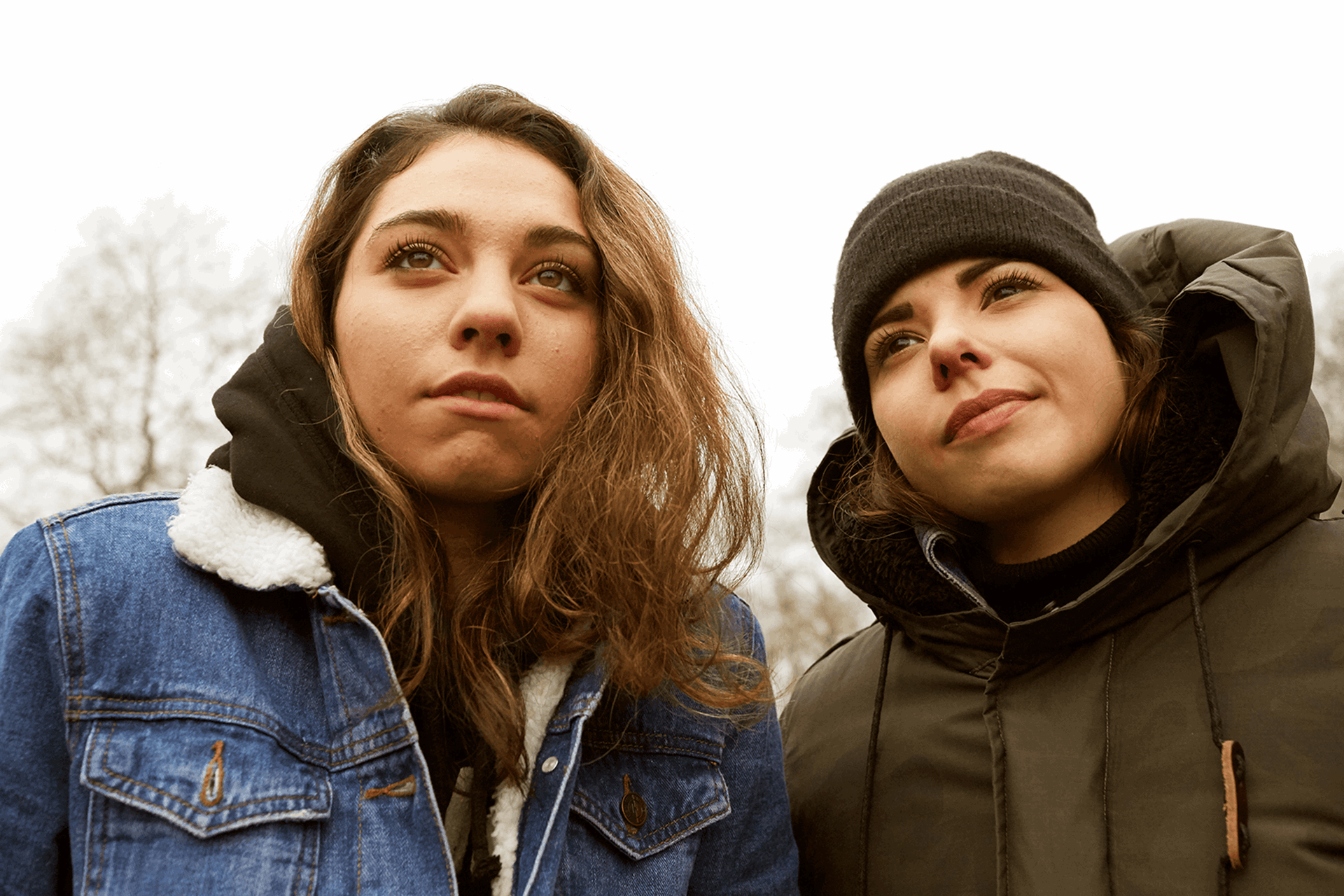 Two young people standing together and looking up at something.