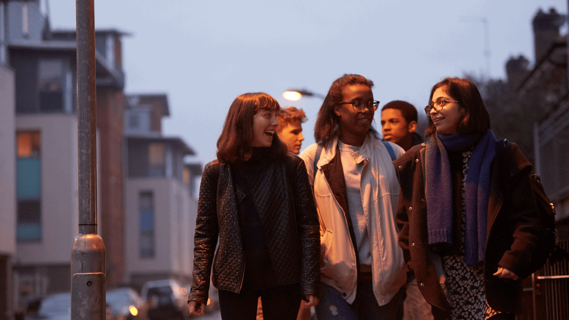 wide-shot-of-a-group-of-young-people-smiling-while-walking-on-a-street-with-houses-at-night