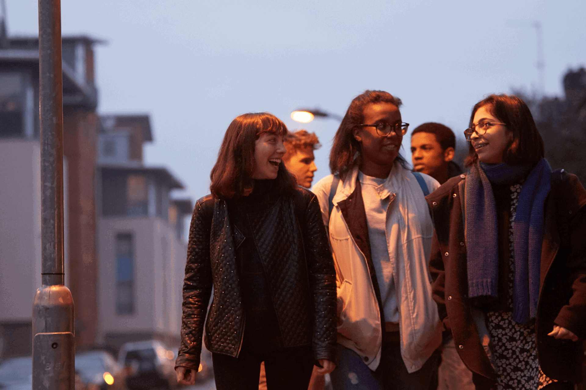 wide-shot-of-a-group-of-young-people-smiling-while-walking-on-a-street-with-houses-at-night