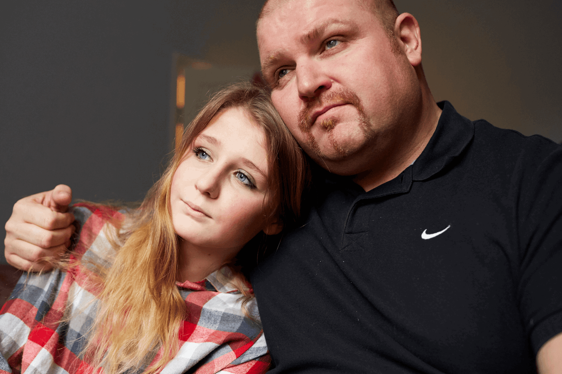 A father with his arm around his young daughter indoors