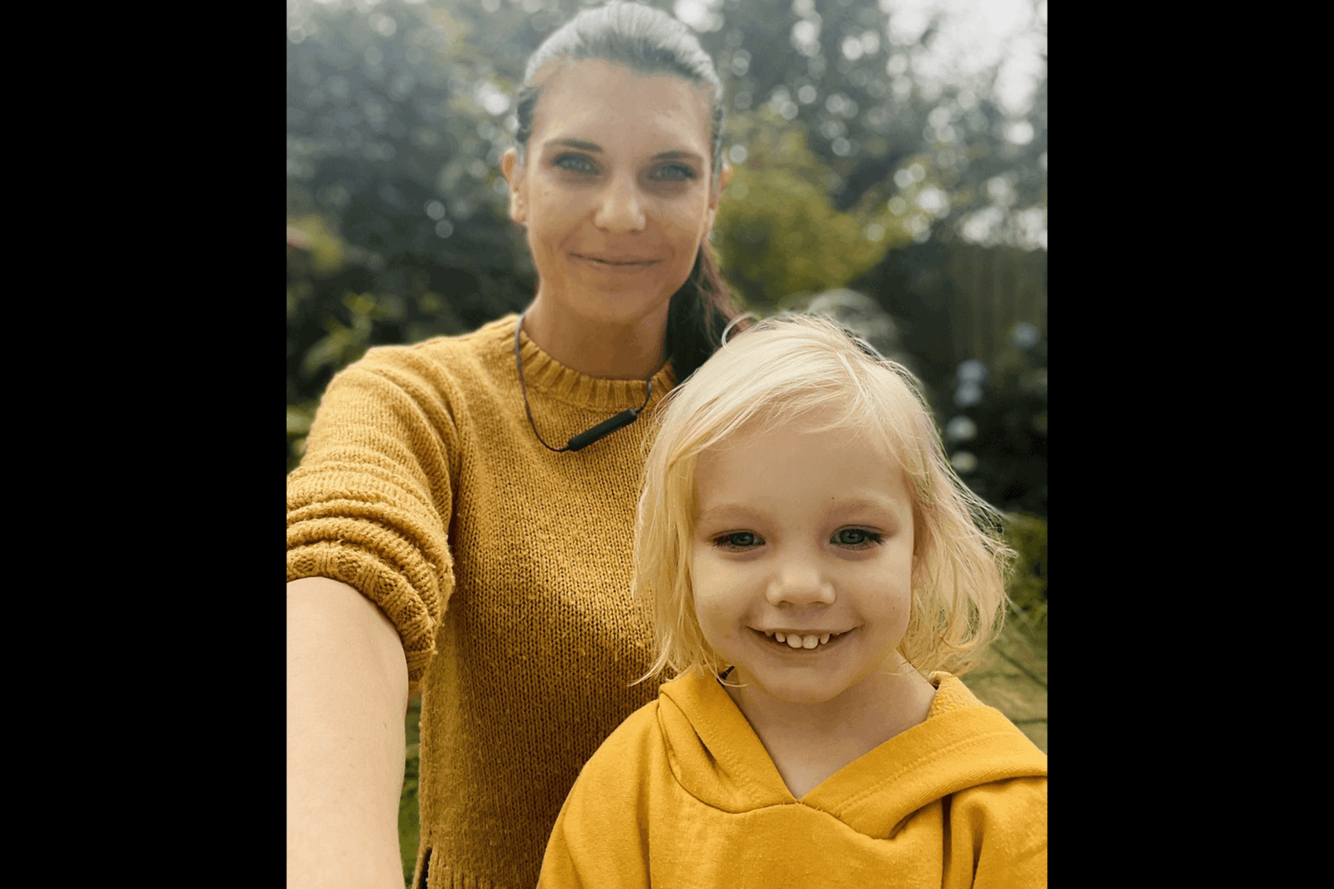 A mother and child smile at the camera wearing a yellow jumper and a yellow hoodie