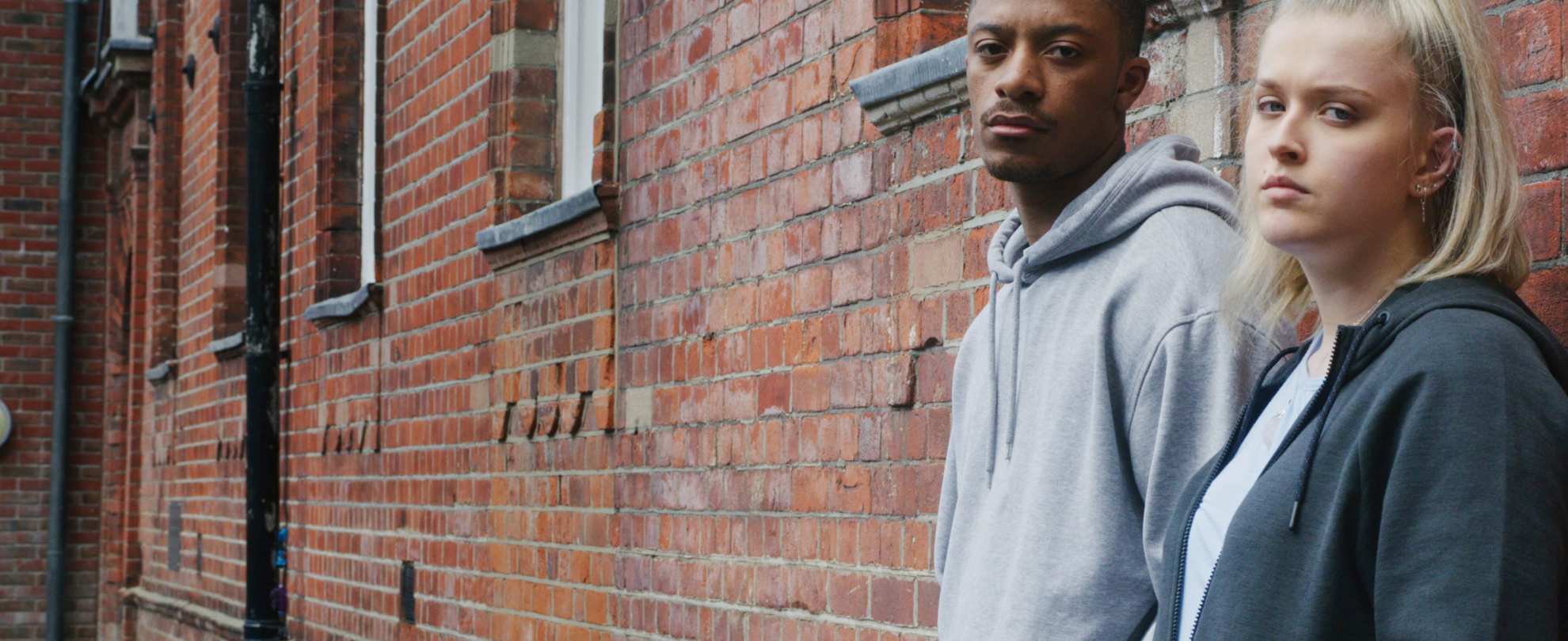 A male and female student leaning against the wall