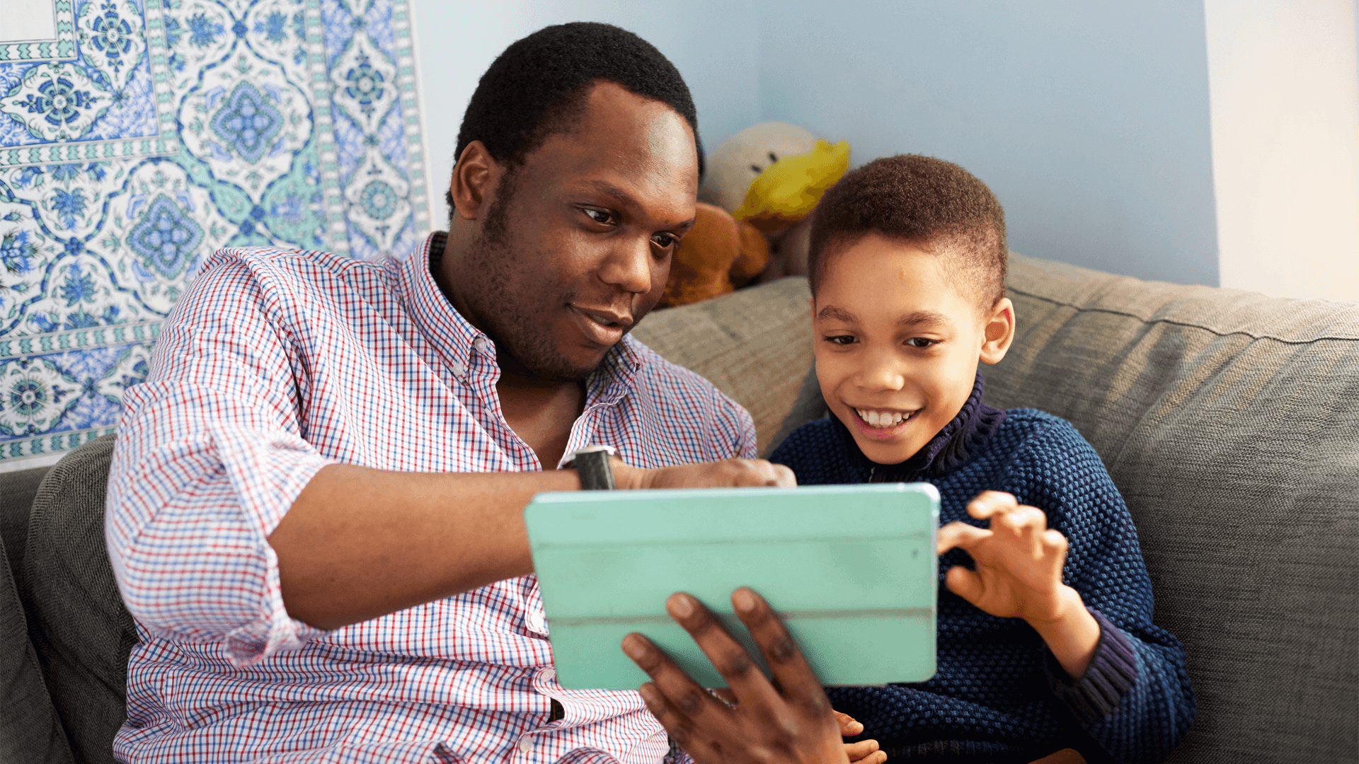 A father and son using a tablet together on the sofa smiling