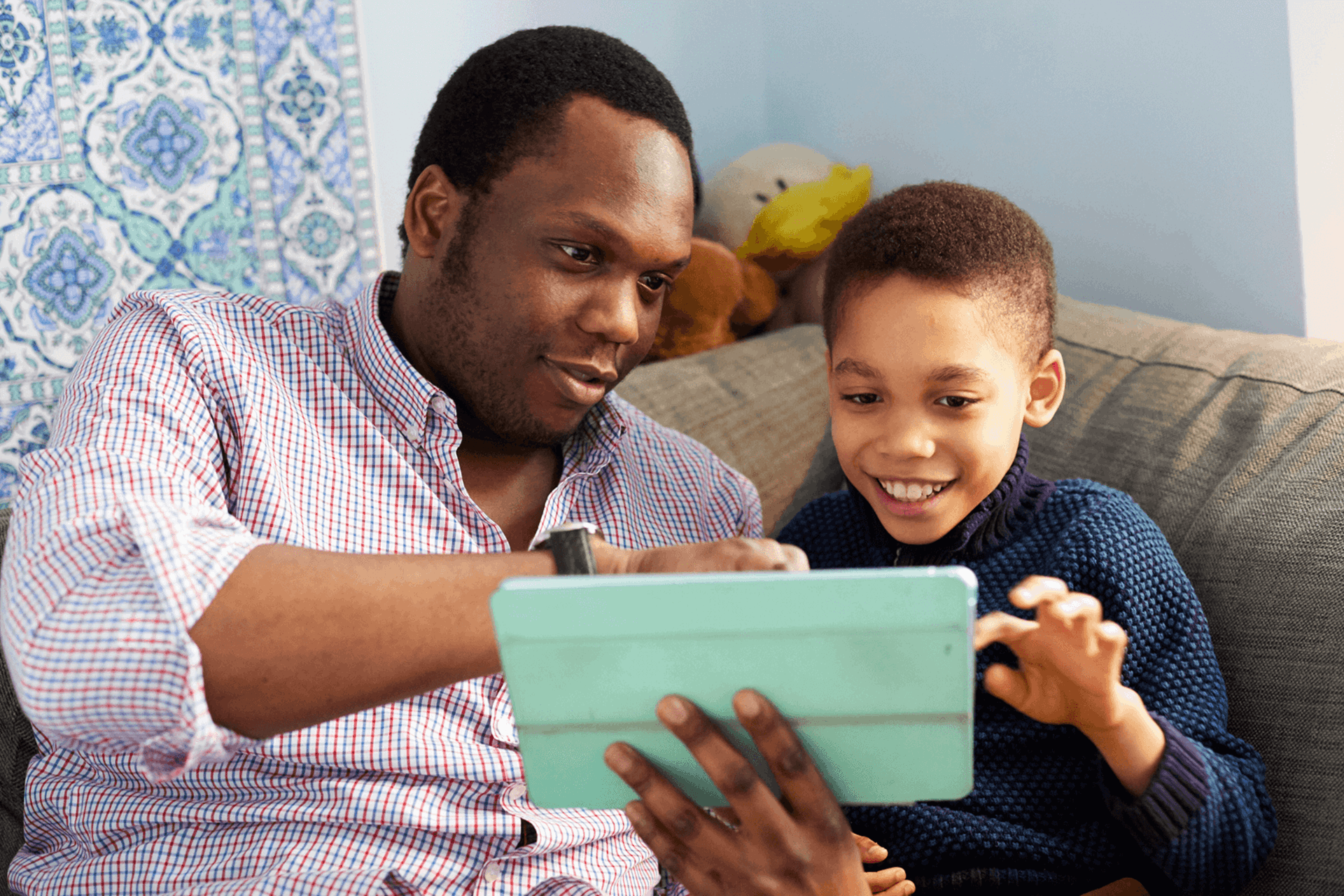 A father and son using a tablet together on the sofa smiling