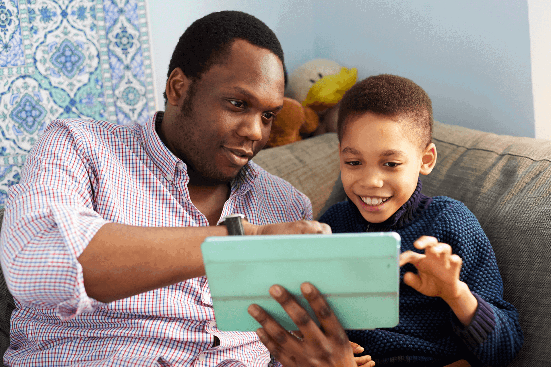 A father and son using a tablet together on the sofa smiling