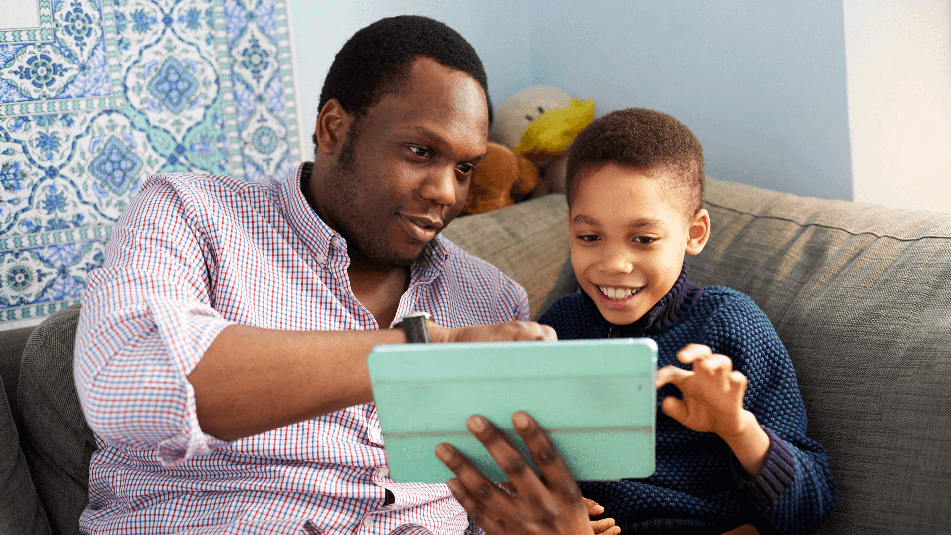 A father and son using a tablet together on the sofa smiling