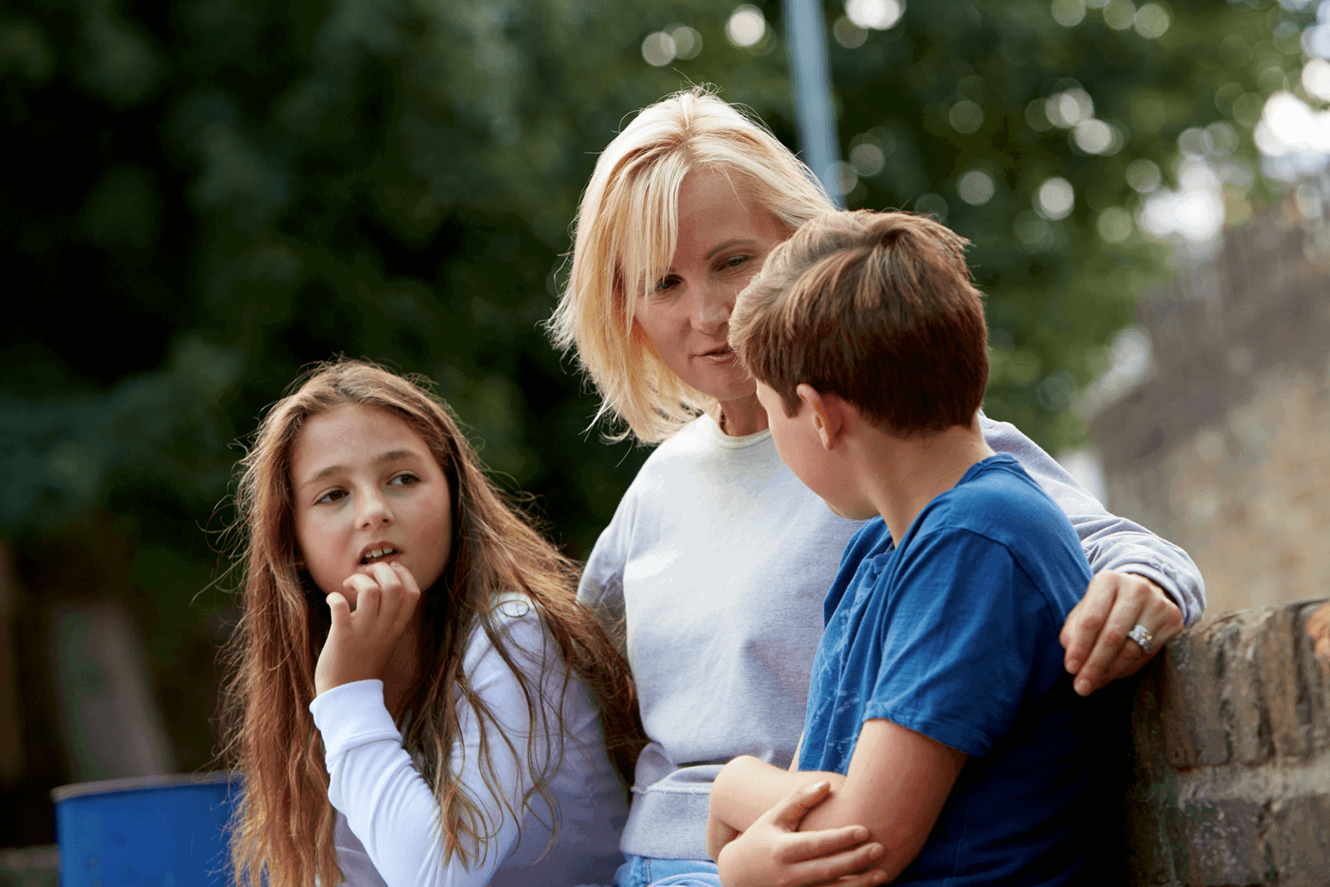 A mother sitting against a wall talking to her children with her arms around them