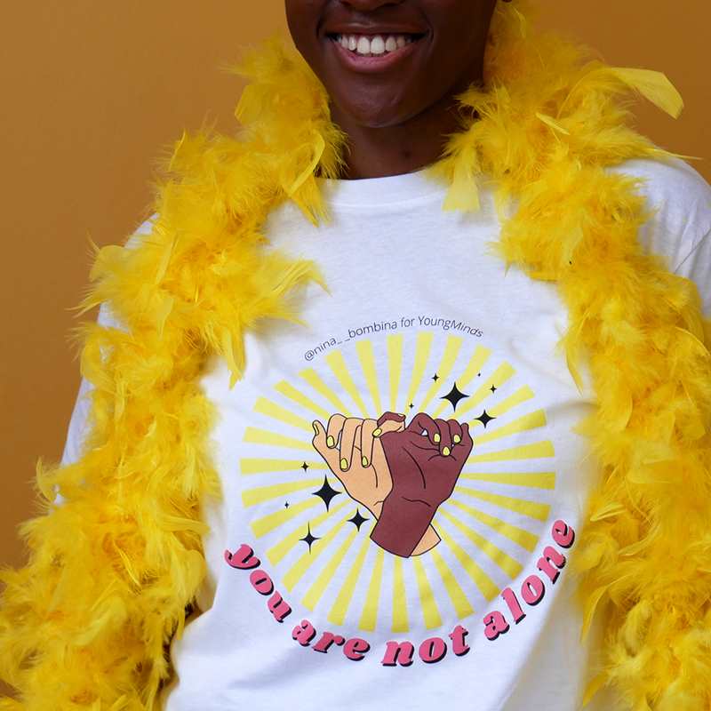 A close up of a woman smiling wearing a yellow feather bower and Nina Bombina bespoke 'You are not alone' graphic #HelloYellow T-shirt