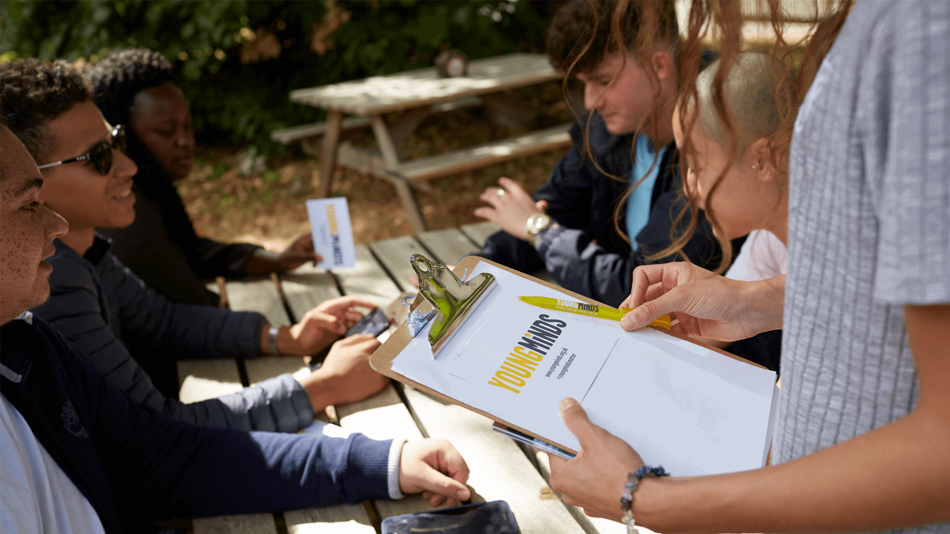 YoungMinds volunteer giving out leaflets to group of students hanging out in campus