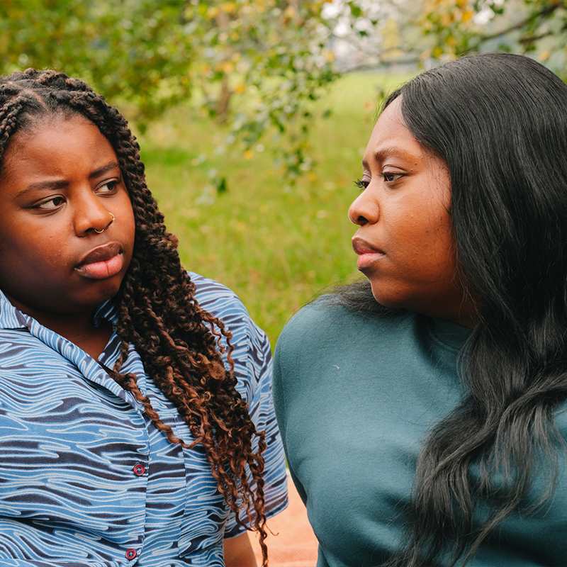 A young Black woman talking about something serious with an older Black woman in the park.