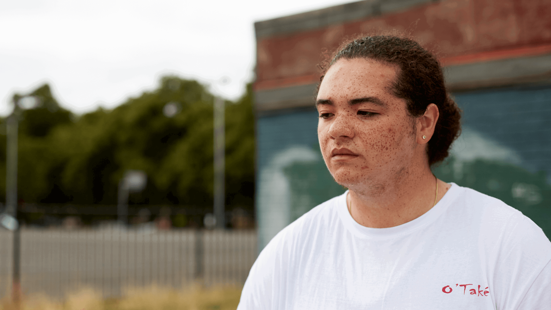 medium shot of a boy with curly hair wearing white shirt thinking seriously with a building on the background