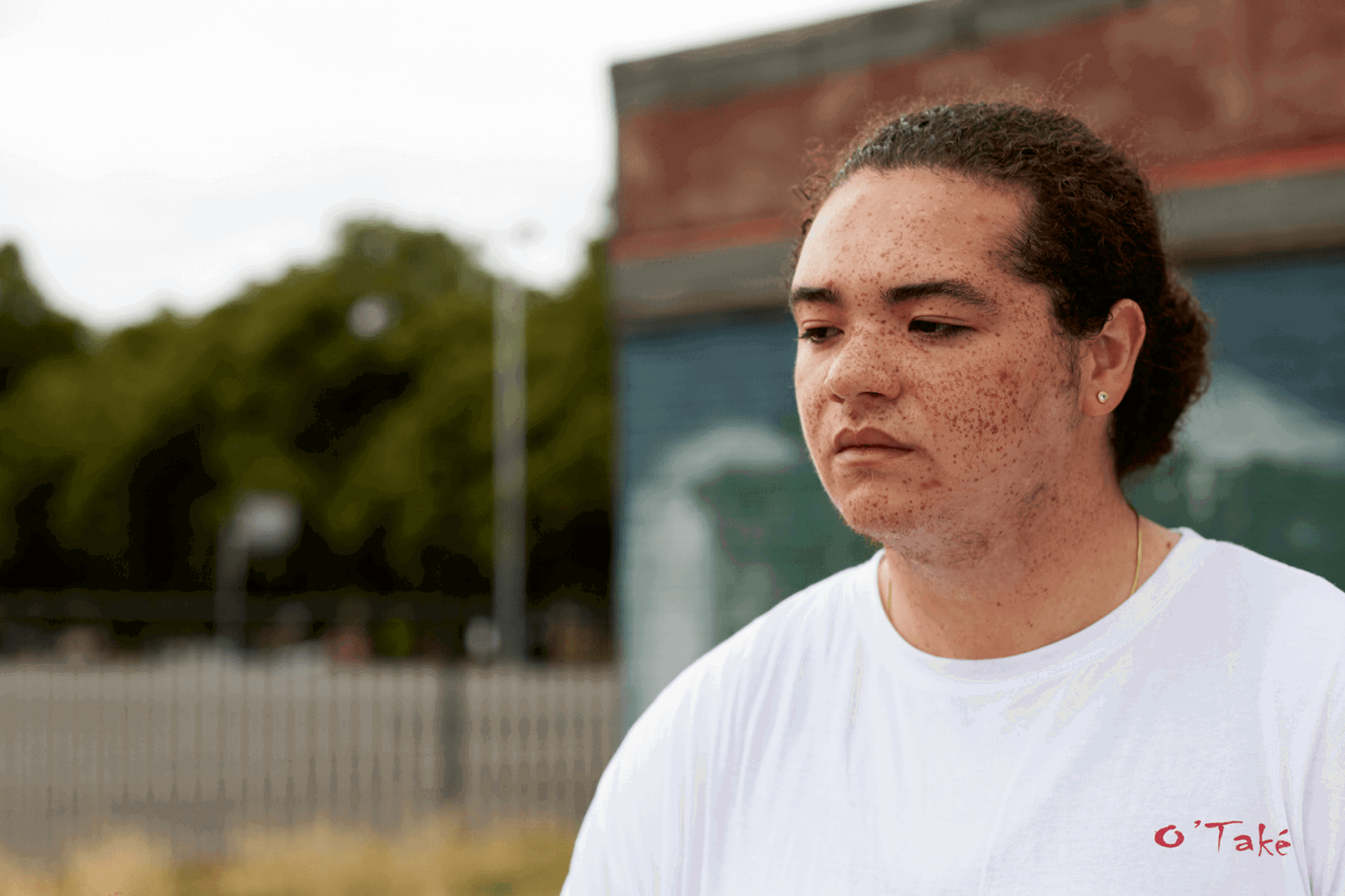 medium shot of a boy with curly hair wearing white shirt thinking seriously with a building on the background