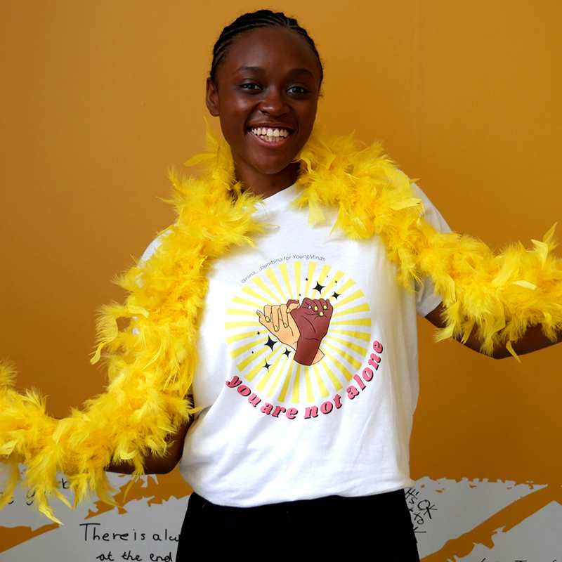 A woman smiling wearing a yellow feather bower and Nina Bombina bespoke 'You are not alone' graphic #HelloYellow T-shirt