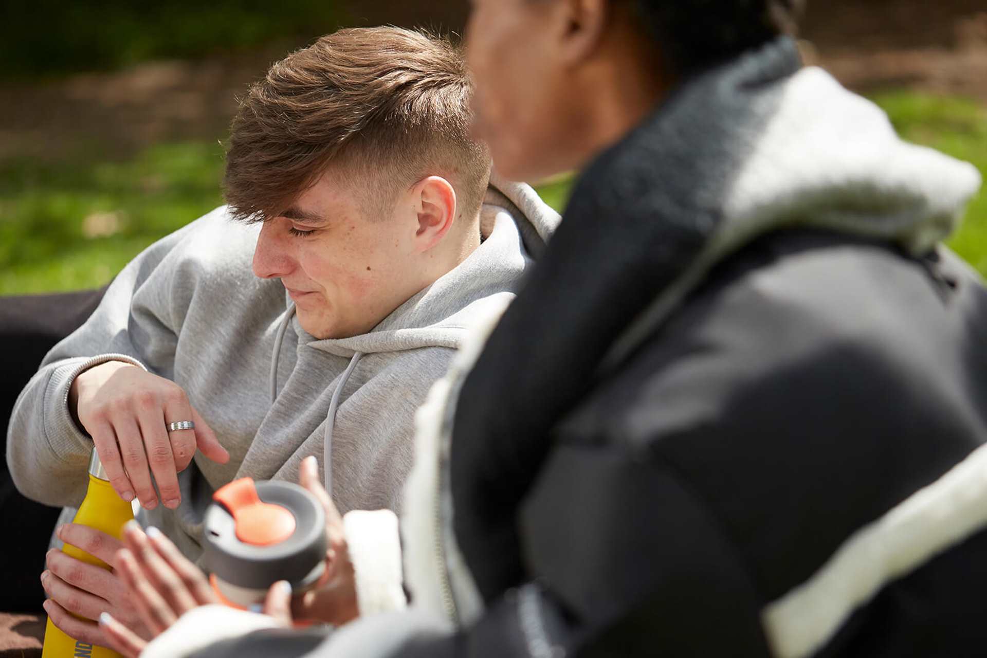 Two young people sitting on the grass together in a park.