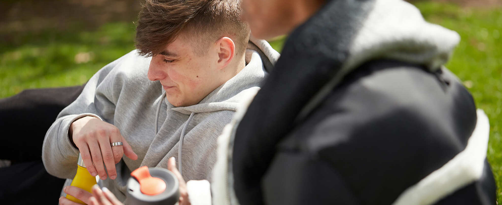 Two young people sitting on the grass together in a park.