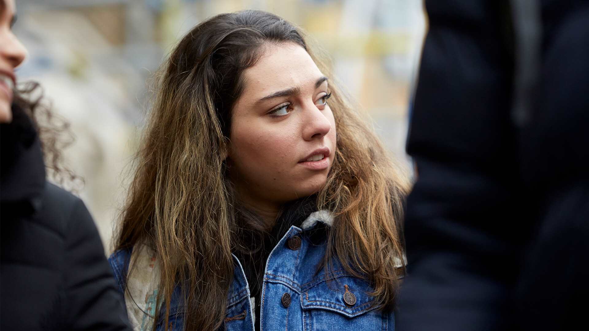 A young person looks away while she stands between two other young people.