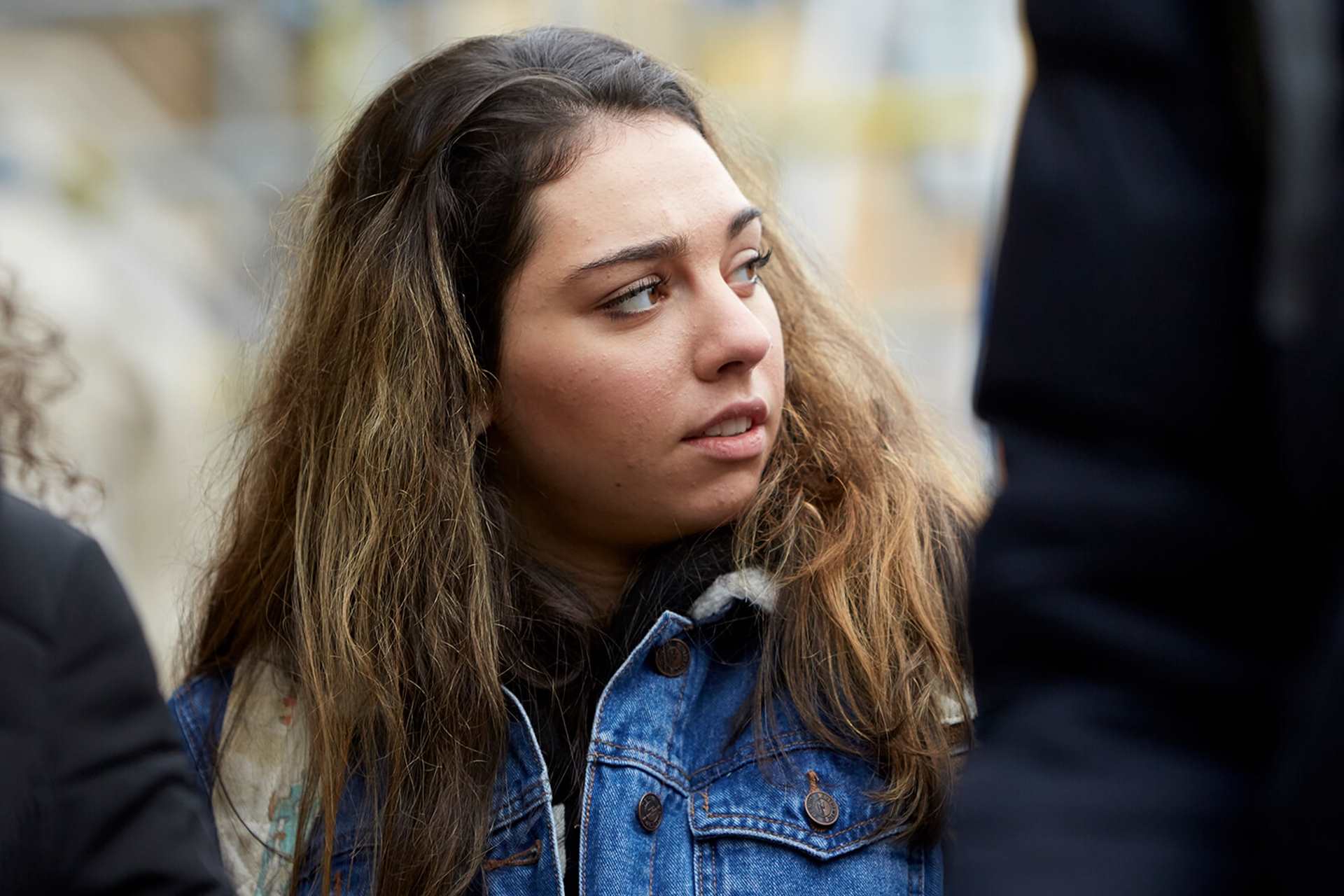 A young person looks away while she stands between two other young people.