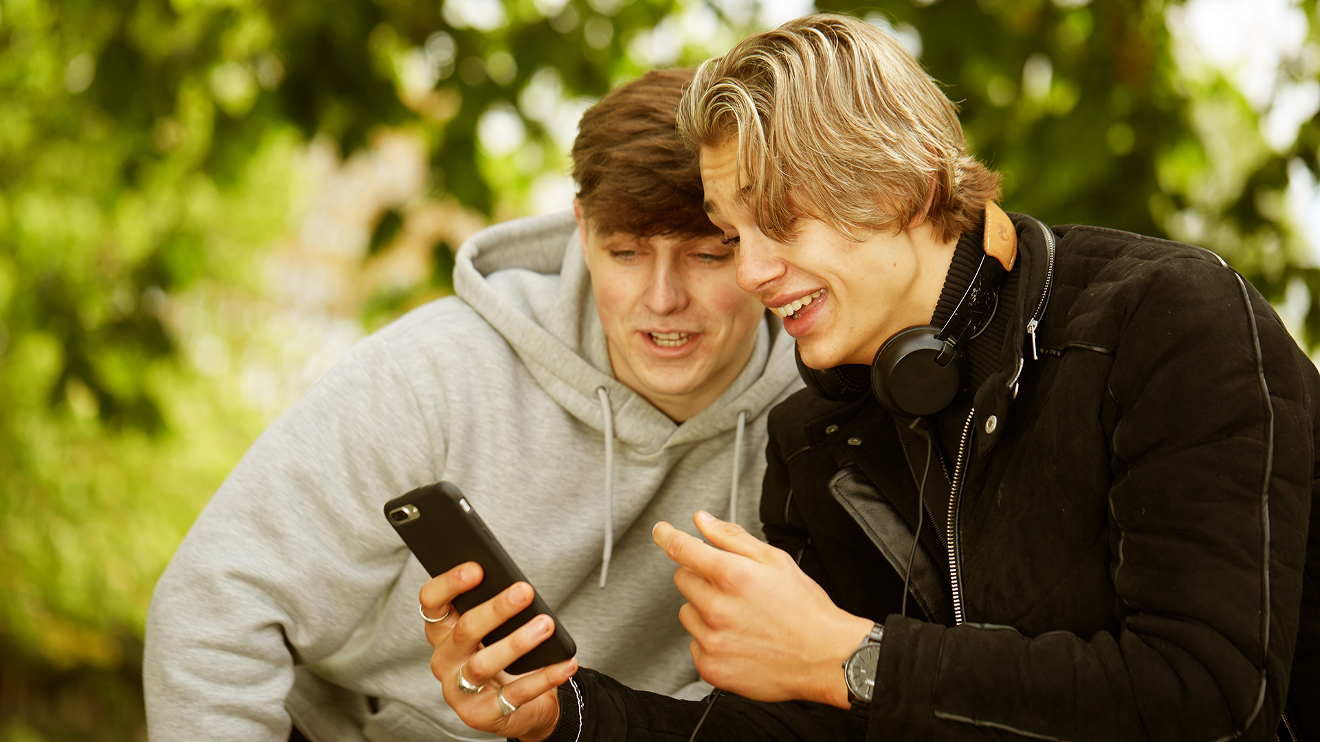 Two boys looking at a phone and smiling in the park.