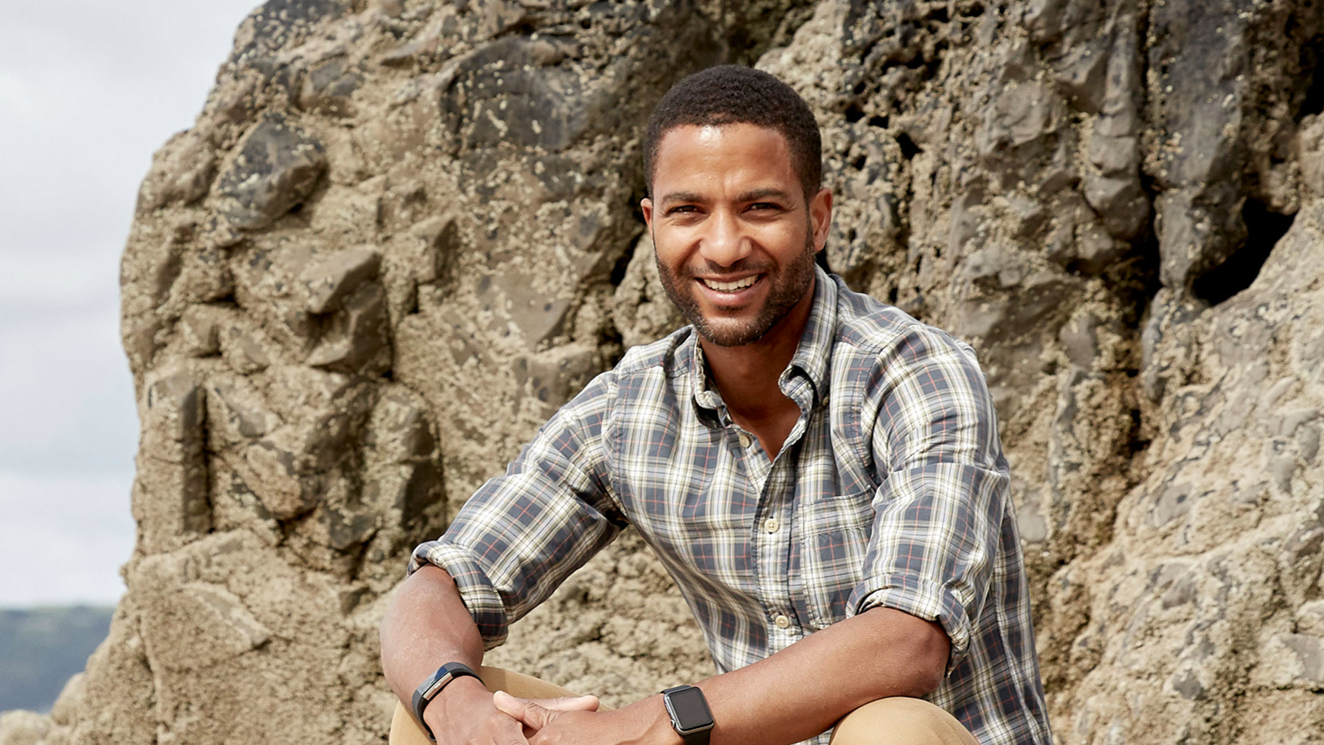 Sean Fletcher smiling and sitting on a rock by the coast