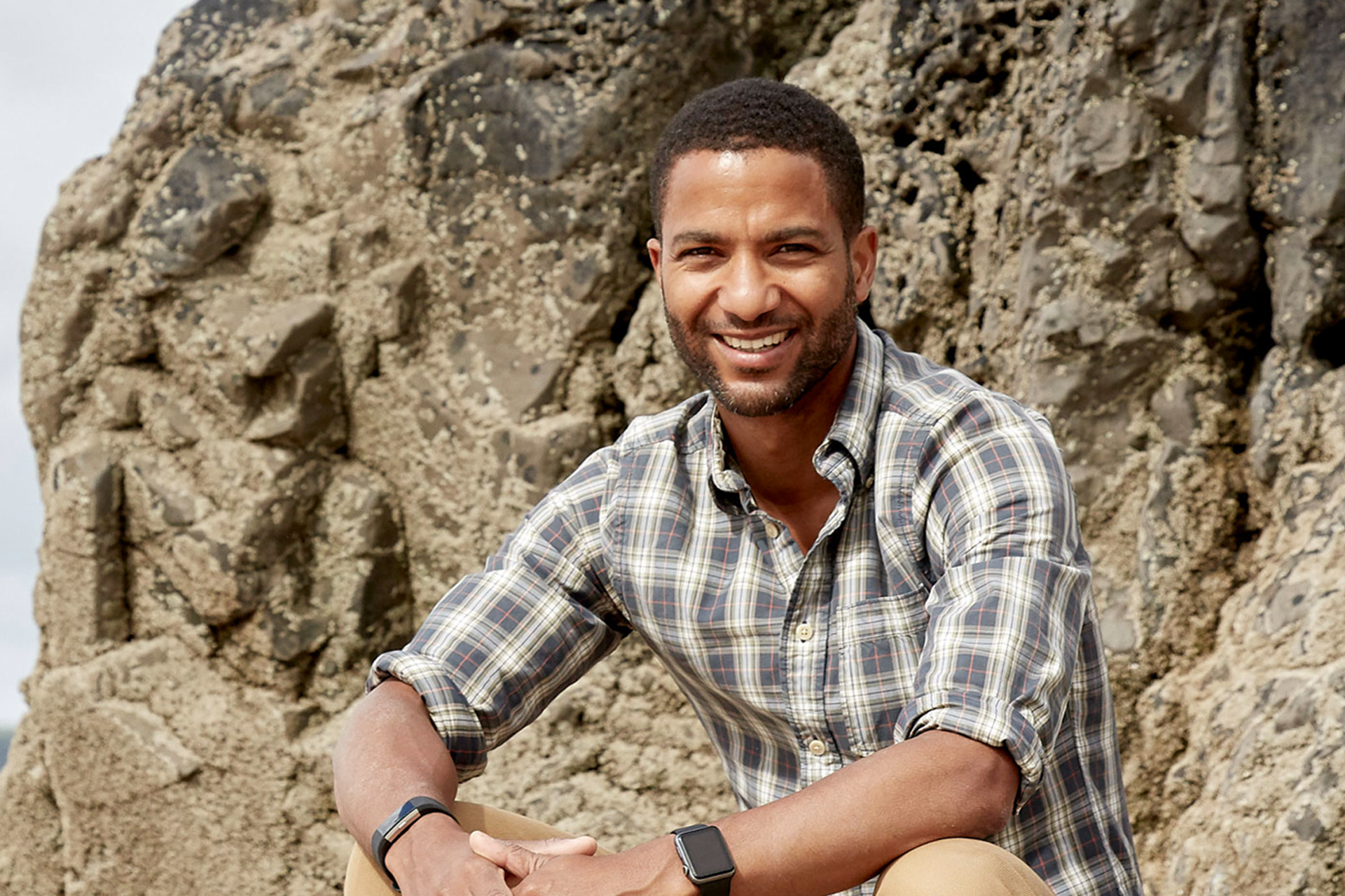 Sean Fletcher smiling and sitting on a rock by the coast
