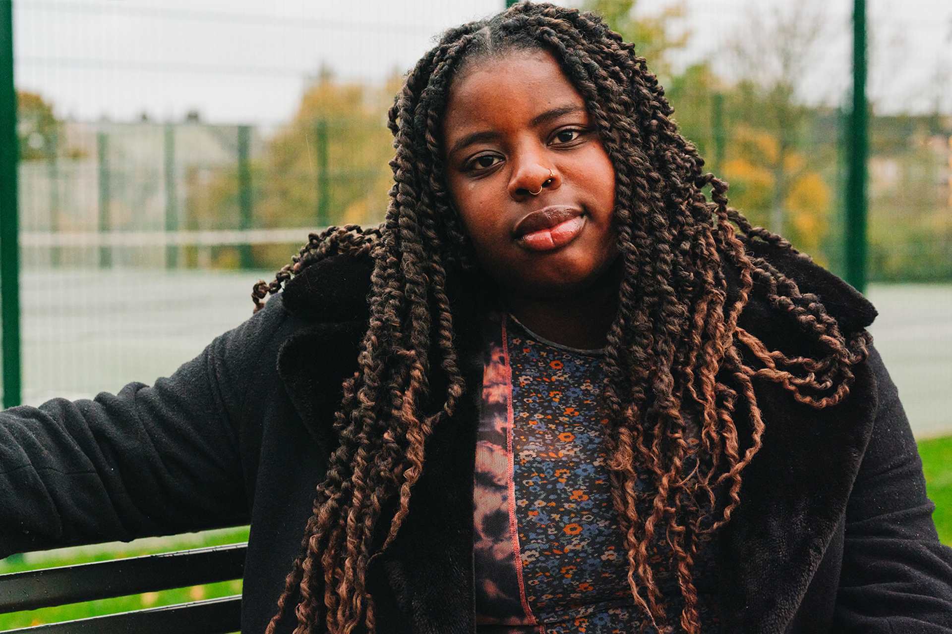 A young Black woman sitting on a bench in the park.