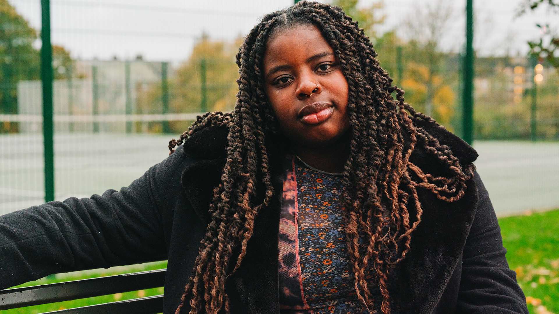 A young Black woman sitting on a bench in the park.